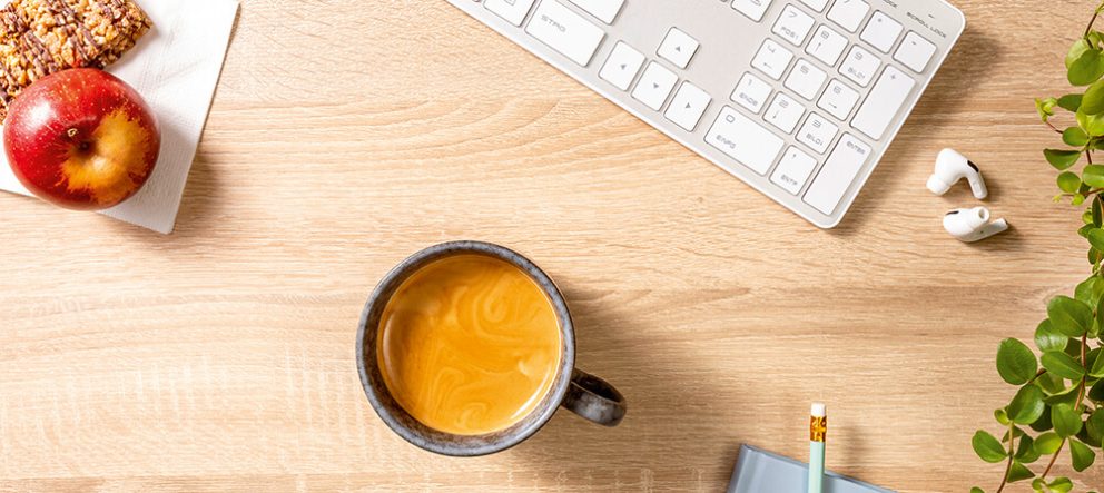 Tasse Kaffee, Apfel, Tastatur und Kopfhörer auf Holztisch aus der Vogelperspektive