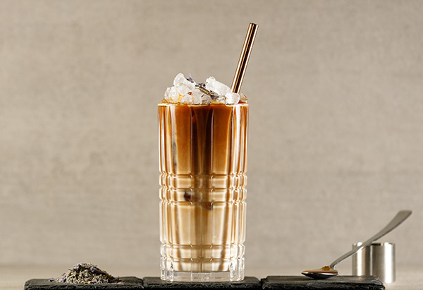 Erfrischendes Kaltgetränk "Bees and Beans" mit doppeltem Espresso, Haferdrink und Lavendelhonig in einem Glas serviert.